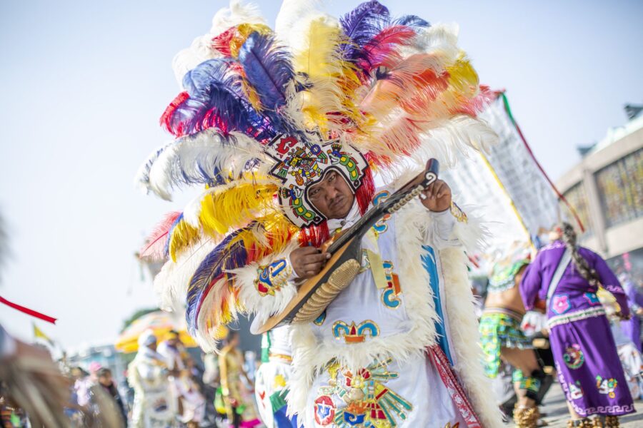 Danzante con penacho de plumas de colores tocando un instrumento de cuerda