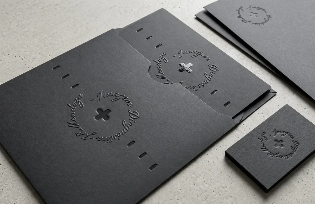 Carpeta, sobre y tarjetas negras con el símbolo de cruz y el texto circular de Julio Mendoza, impresos en relieve.