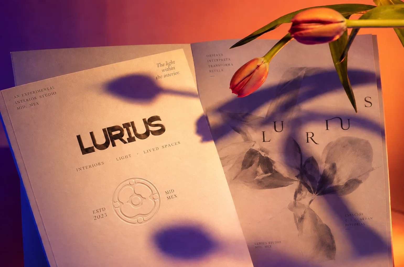 Piezas editoriales de Lurius con el logotipo, el emblema circular y tipografía serif, iluminadas con luz cálida y sombras de flores.