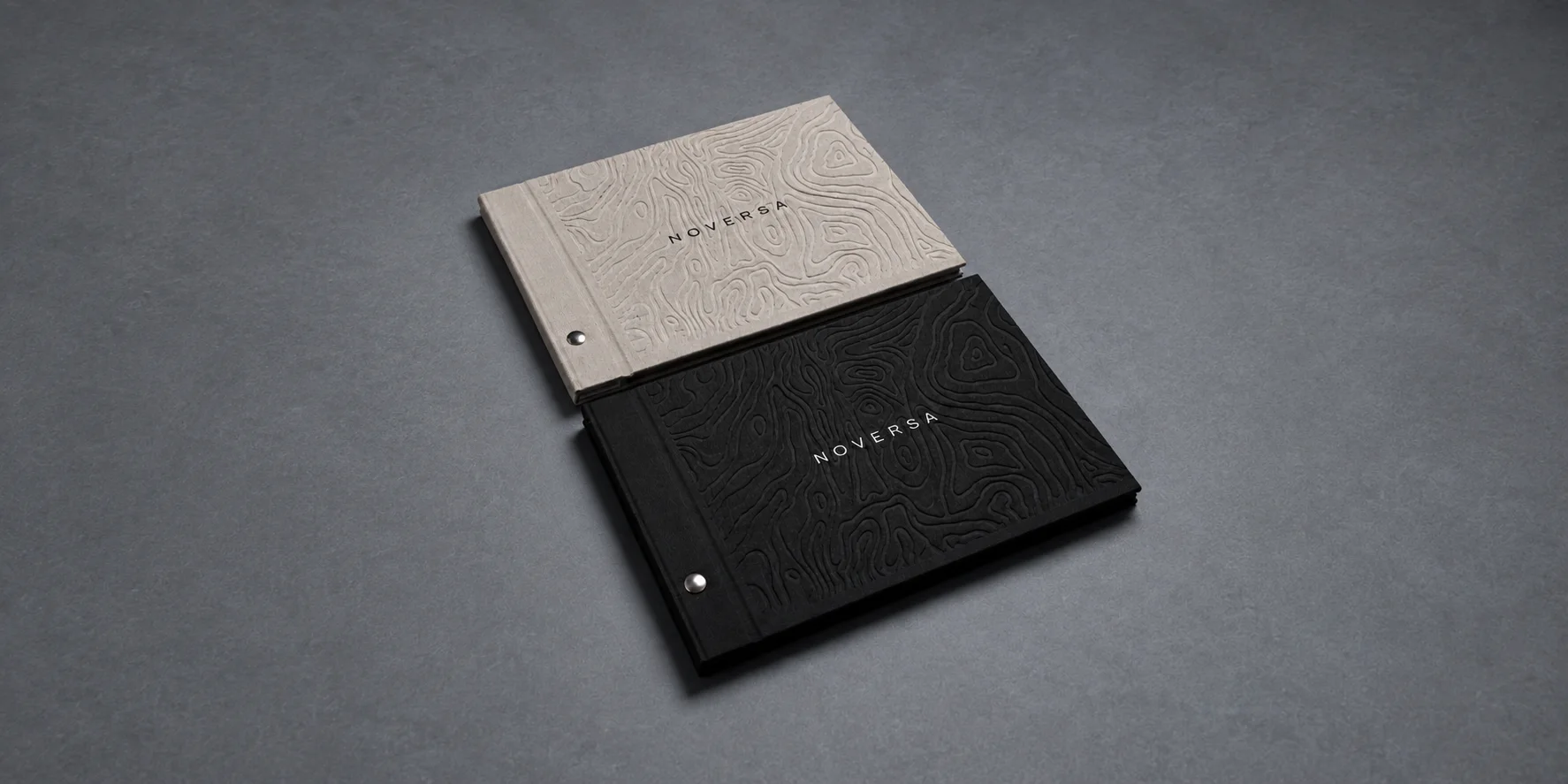 Dos cuadernos de Noversa, uno claro y otro negro, con relieve topográfico y el nombre grabado.
